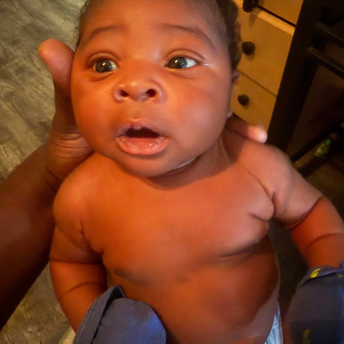 Xzayvion is registered to the contest to win money with this photo: baby, child, infant, hand, mittens, blue_mittens, diaper, face, eyes, mouth, skin, curly_hair, wooden_drawer, floor, indoor, person, expression, portrait, candid, holding