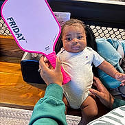 Xzayvion joined the competition — help win amazing prizes! baby, child, person, pickleball_paddle, sports_court, green_sweatshirt, gray_onesie, hand, face, indoor, bench, wood, netting, blue_sock, backpack, table, colorful, sport, cute, seated