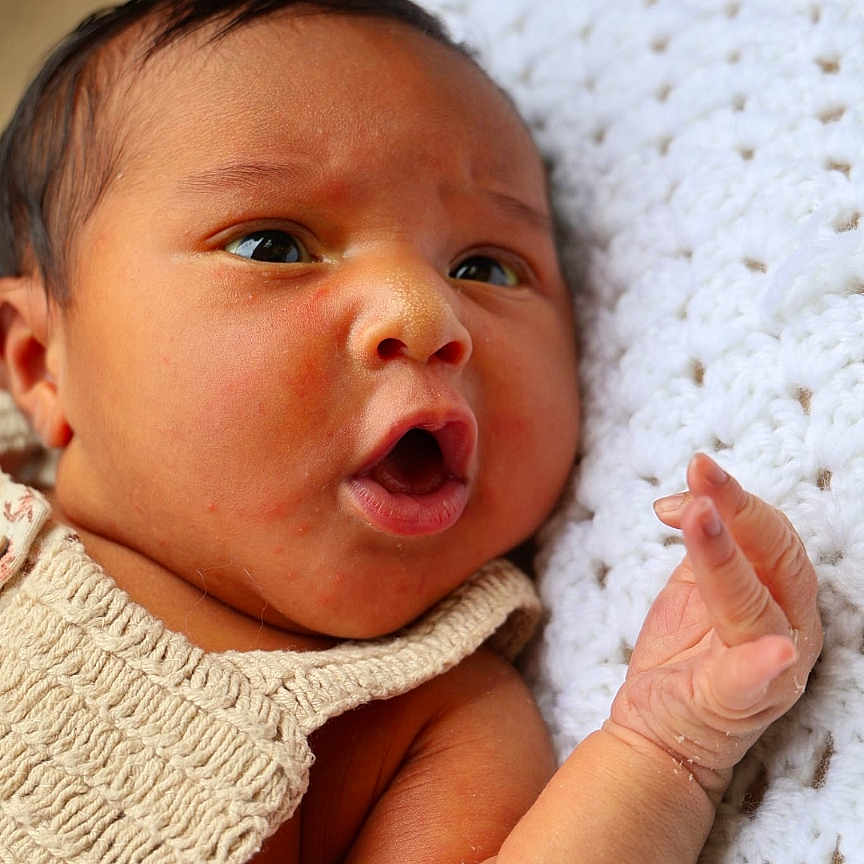 Aiyah is registered to the contest to win money with this photo: baby, blanket, child, close_up, curious, cute, cute_face, expression, face, hand, indoors, infant, knitwear, lying_down, newborn, person, portrait, skin, soft_texture, young