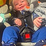 baby, infant, child, car_seat, seat_belt, buckle, smile, happy, plush_toy, stuffed_animal, elephant_plush, blue_pants, sneakers, plaid_shirt, hands, face, close_up, portrait, interior, cozy