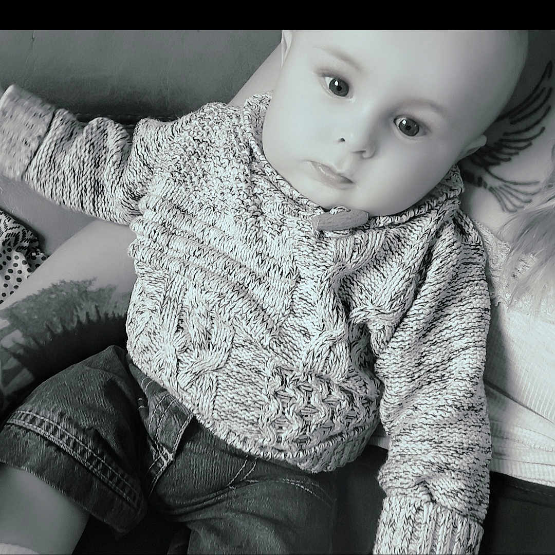 Gabriel participe au concours pour gagner de l'argent avec cette photo : arm, baby, casual_clothing, child, closeup, cute, denim_pants, eyes, face, hands, indoor, infant, knitted_sweater, monochrome, person, portrait, relaxed, seated, soft_lighting, tattoo