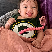 Shay joined the competition — help win amazing prizes! baby, child, tongue_out, blanket, pacifier, clothing, smile, happy, face, person, indoors, cute, wrapped, pink, green, logo, hand, portrait, infant, cozy