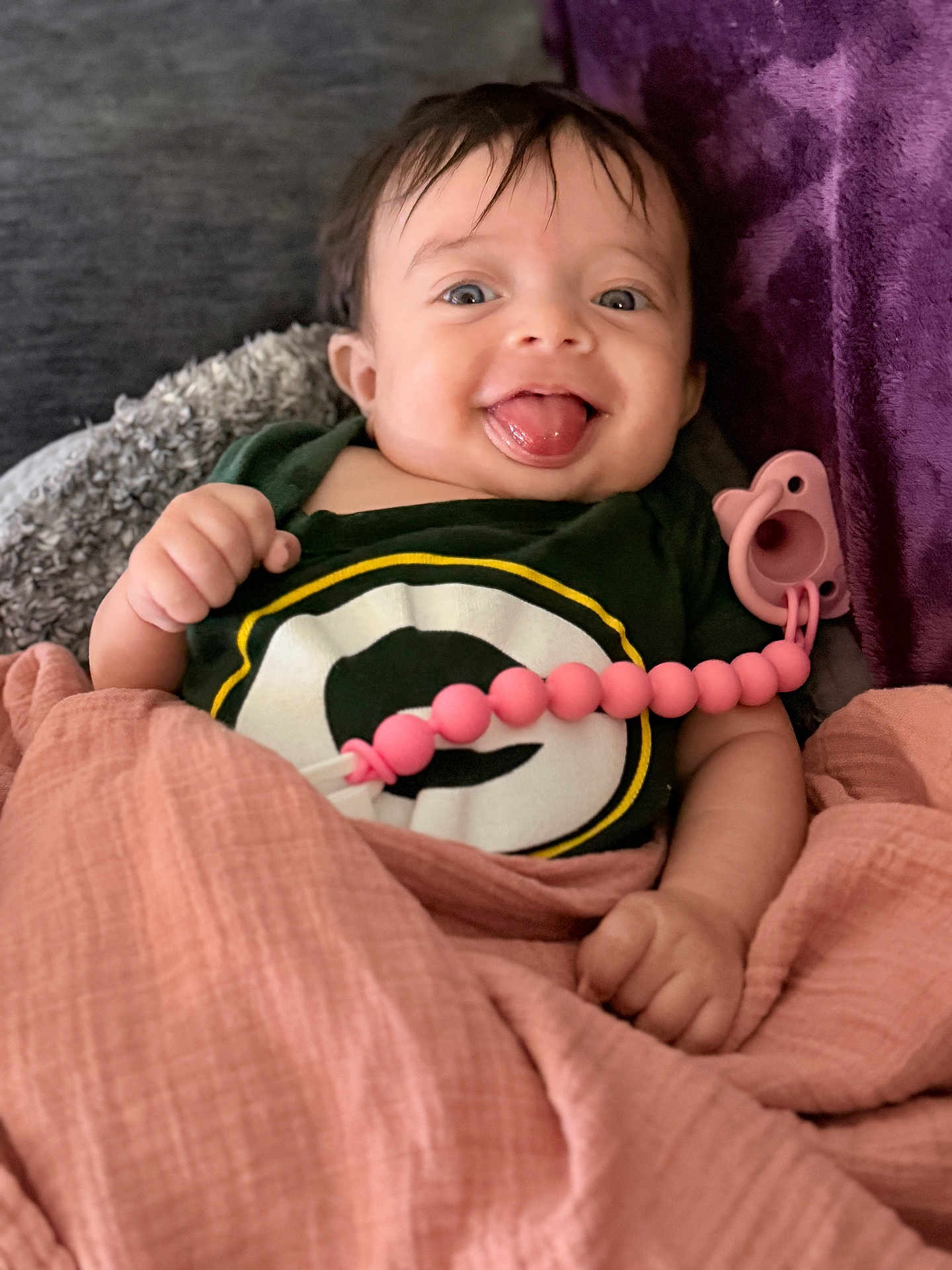 Shay joined the competition — help win amazing prizes! baby, child, tongue_out, blanket, pacifier, clothing, smile, happy, face, person, indoors, cute, wrapped, pink, green, logo, hand, portrait, infant, cozy