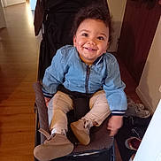 Gabriel a rejoint le concours — aidez-le/la à gagner de superbes lots ! child, toddler, baby, stroller, smiling, indoor, jean_jacket, curly_hair, brown_shoes, socks, wooden_floor, hallway, doorway, coat, seat_belt, portrait, happy, sneakers, shoe_rack, stroller_seat