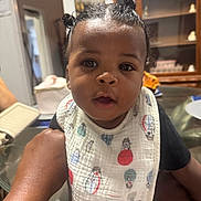 Atlas joined the competition — help win amazing prizes! baby, child, infant, portrait, face, eyes, curious, indoors, home, bib, clothing, hair_buns, sitting, being_held, adult_arm, furniture, cabinet, dining_room, smiling, photography