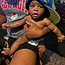 Atlas is registered to the contest to win money with this photo: baby, infant, child, portrait, indoor, being_held, blue_hat, baseball_cap, sideways_hat, wide_eyed, open_mouth, smiling, adult, parent, georgia_shirt, sportswear, diaper, family, candid, home