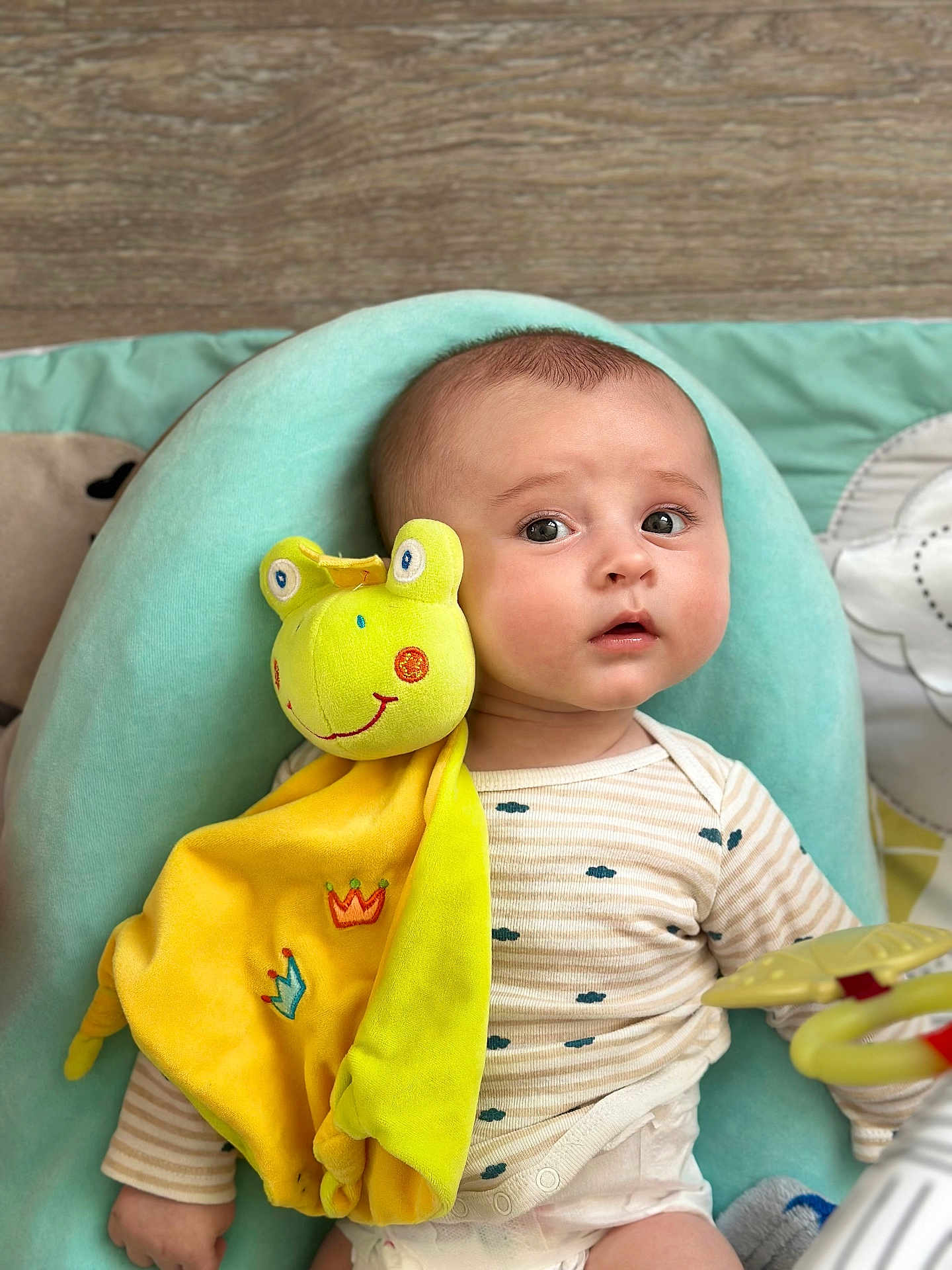 Hardin participe au concours pour gagner de l'argent avec cette photo : baby, plush_toy, frog, cushion, onesie, striped_clothing, indoor, child, infant, soft_toy, expression, curious, reclining, fabric, colorful, cute, comfort, portrait, hand, floor