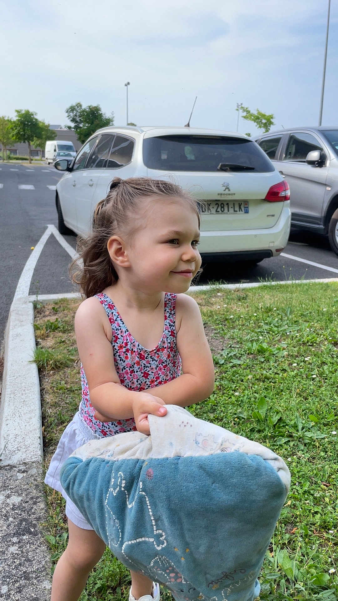 Leïla participe au concours pour gagner de l'argent avec cette photo : child, smiling, outdoor, blanket, grass, car, parking_lot, person, shorts, sleeveless_top, playful, happy, young, curly_hair, side_view, daytime, casual_clothing, holding, nature, greenery
