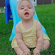 Blessing joined the competition — help win amazing prizes! baby, child, grass, slide, playground, outdoor, yellow_dress, headband, smiling, happy, barefoot, summer, toy, fence, blue_slide, infant, cute, sitting, nature, daytime