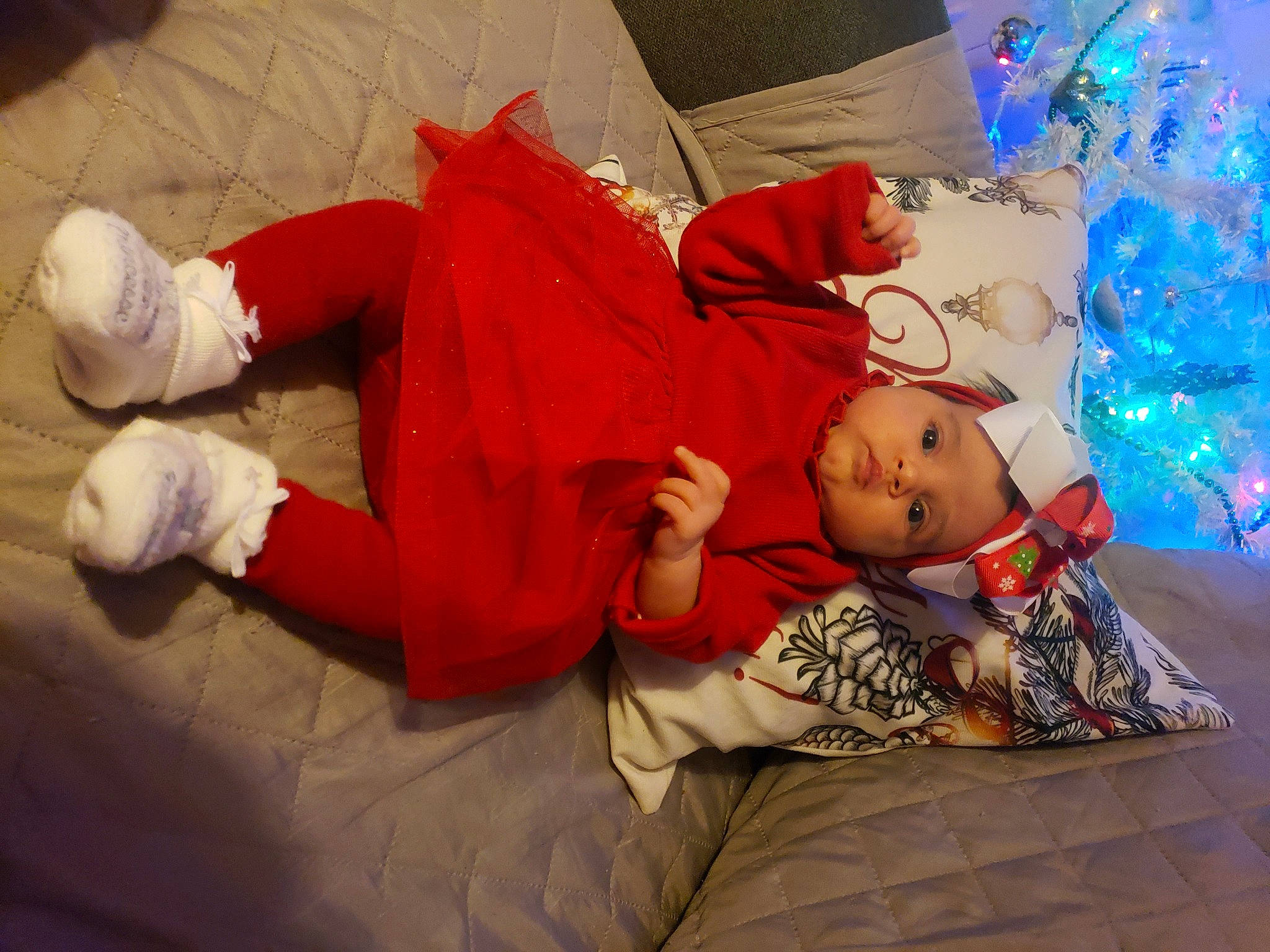 Emily a rejoint le concours — aidez-le/la à gagner de superbes lots ! baby, baby_toddler_clothing, child, christmas_eve, christmas_ornament, christmas_tree, comfort, event, flooring, fun, happy, headwear, holiday, human_leg, knee, lap, leg, person, sitting, sock