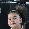 Mady a rejoint le concours — aidez-le/la à gagner de superbes lots ! child, girl, curly_hair, headband, yellow_shirt, floral_pattern, car_interior, car_seat, backseat, portrait, smiling, young_child, casual_clothing, daylight, window, seat_headrest, human, person, indoor, candid