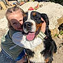 Ruby participe au concours pour gagner de l'argent avec cette photo : child, dog, bernese_mountain_dog, hugging, smiling, outdoor, sunlight, rocks, wooden_structure, happy, pet, casual_clothing, green_jacket, white_shoes, nature, friendship, tongue_out, playful, close_up, daylight