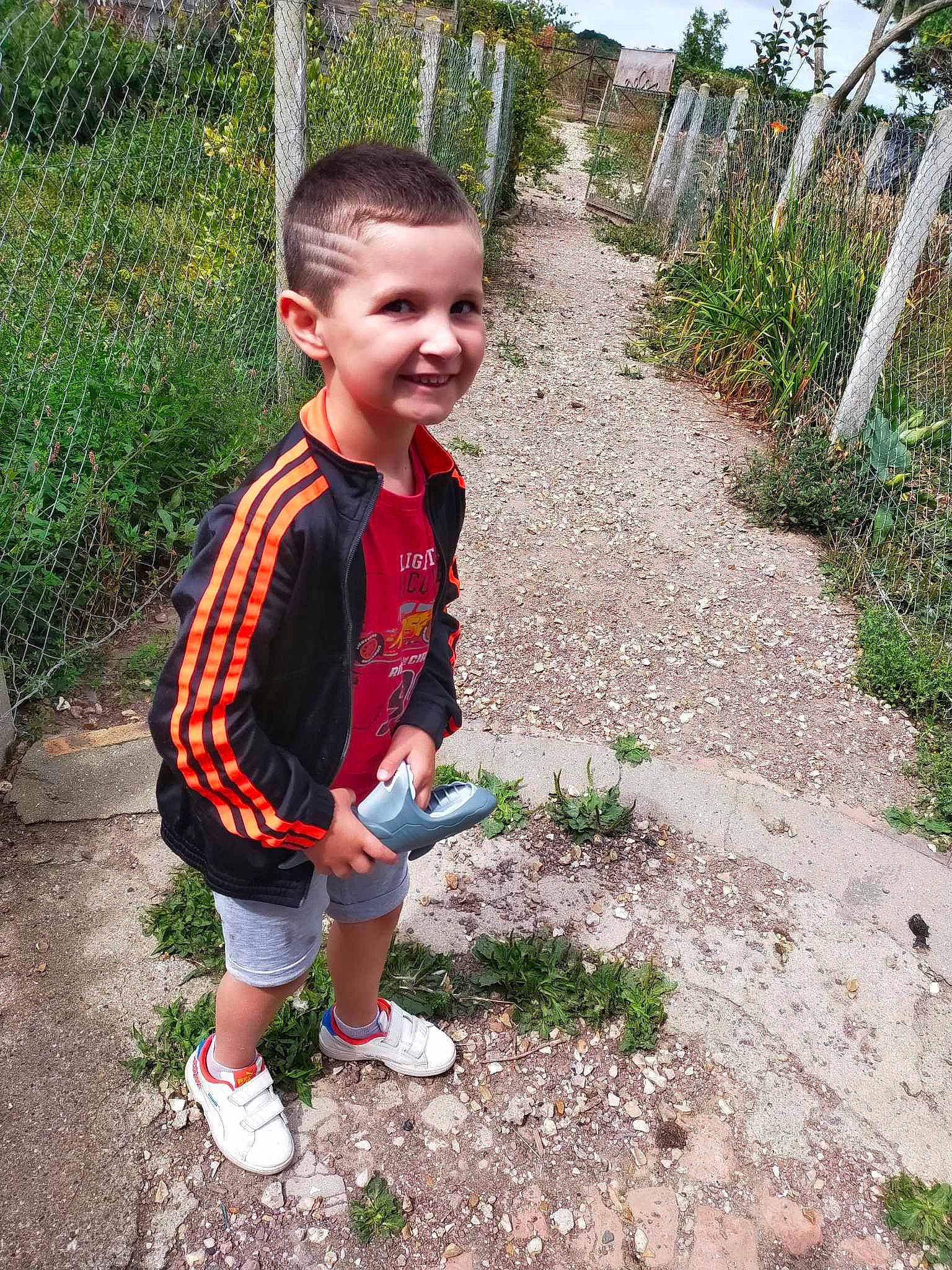 Leo participe au concours pour gagner de l'argent avec cette photo : baby_toddler_clothing, boot, fence, fun, garden, grass, happy, joy, landscape, leisure, pattern, people_in_nature, person, plant, play, sandal, shorts, smile, soil, t_shirt