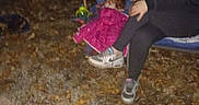 Rory is registered to the contest to win money with this photo: night, outdoor, child, toddler, girl, camping_chair, jacket, pink_jacket, gravel, fallen_leaves, tiki_torch, toy, sneakers, casual_clothing, young_person, dark_background, nature, sitting, people, autumn