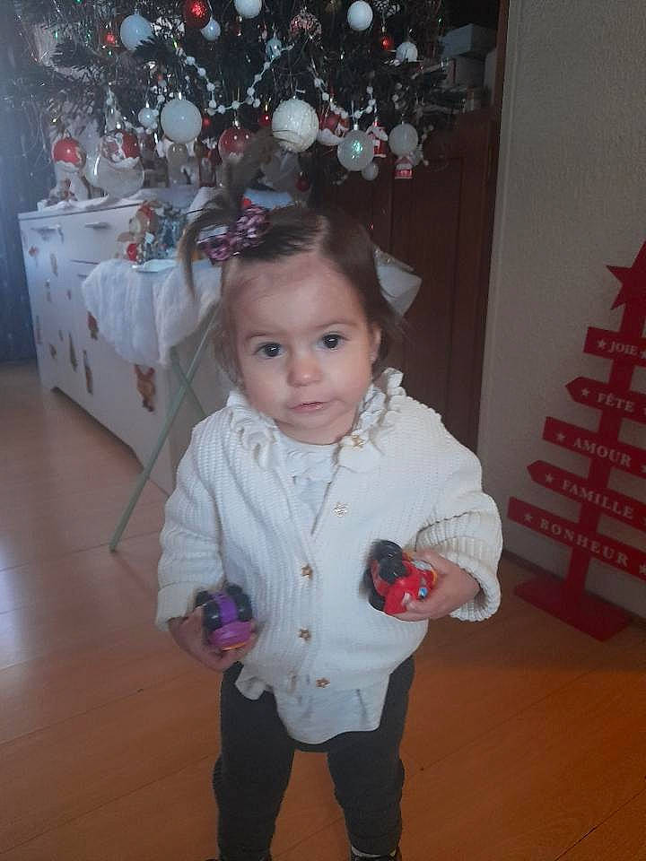 Anastazia a rejoint le concours — aidez-le/la à gagner de superbes lots ! baby_toddler_clothing, christmas_ornament, christmas_tree, eye, facial_expression, flooring, fun, hair, hairstyle, happy, head, human_body, person, pink, plant, red, sleeve, standing, toddler, white