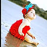 baby, child, red_dress, headband, feathers, beach, sand, water, sitting, cute, portrait, outdoor, infant, funny_face, pouting, photography_watermark, nature, holiday, summer, playful