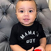 David joined the competition — help win amazing prizes! baby, child, boy, smiling, black_tshirt, red_ball, plush_chair, indoor, cute, happy, portrait, seated, curly_hair, infant, person, hand, face, eyes, skin, clothing