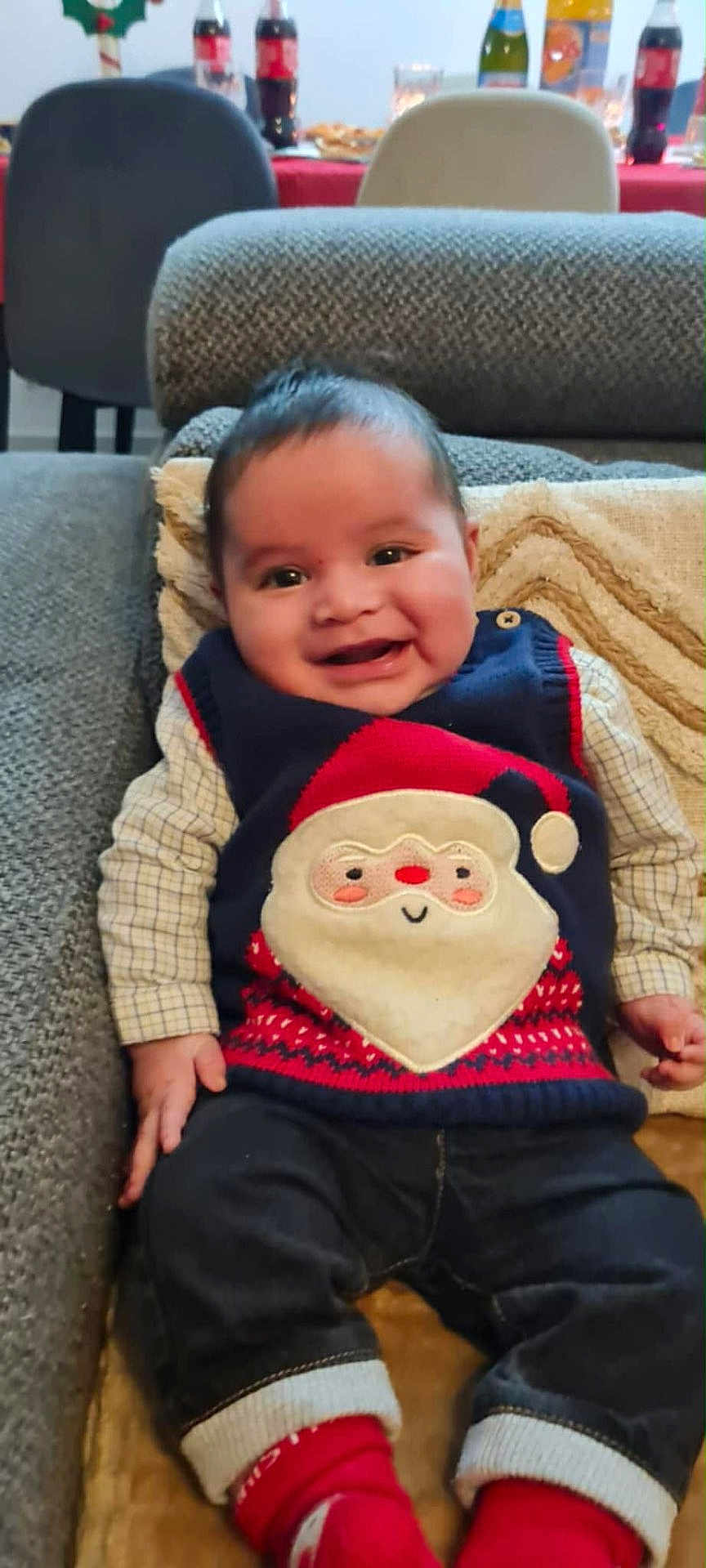 Fares Naël participe au concours pour gagner de l'argent avec cette photo : baby, smiling, sweater_vest, santa_claus, couch, blanket, indoor, child, happy, clothing, red_socks, jeans, face, person, holiday, festive, seated, head, cheerful, cozy