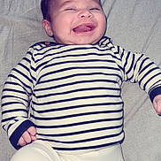Fares Naël participe au concours pour gagner de l'argent avec cette photo : baby, infant, smiling, striped_shirt, white_pants, lying_down, happy, cute, child, face, hands, clothing, fabric, indoor, person, young, cheerful, sleepwear, portrait, toddler
