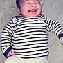 baby, infant, smiling, striped_shirt, white_pants, lying_down, happy, cute, child, face, hands, clothing, fabric, indoor, person, young, cheerful, sleepwear, portrait, toddler