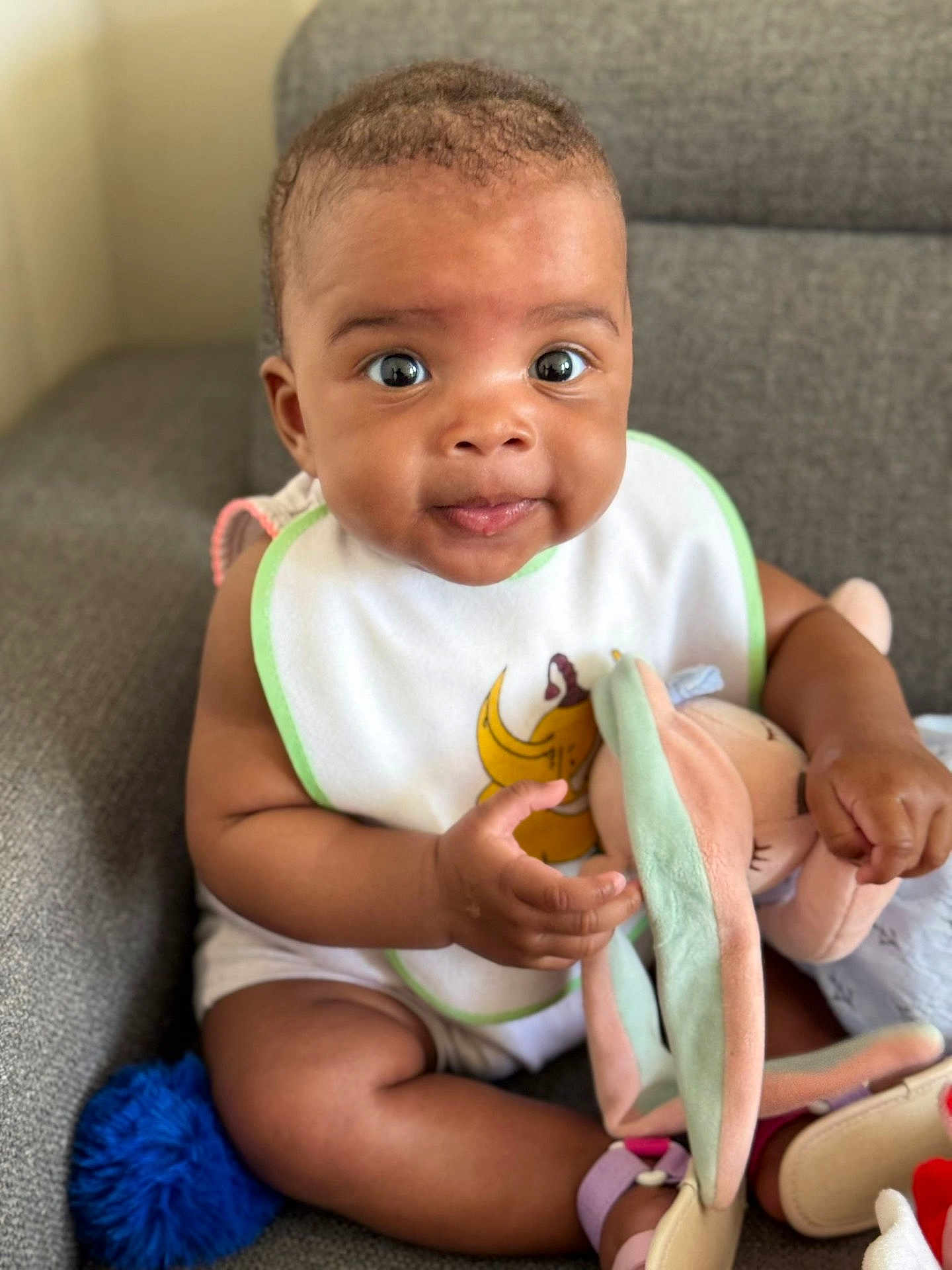 Julianne Kaëla a rejoint le concours — aidez-le/la à gagner de superbes lots ! baby, infant, bib, stuffed_toy, couch, indoor, cute, child, smiling, seated, plush, person, happy, soft_toy, toddler, clothing, skin, hand, footwear, home