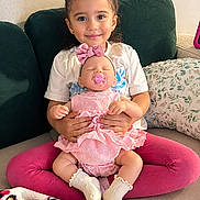 Karla joined the competition — help win amazing prizes! child, girl, toddler, doll, baby_doll, smiling, portrait, sitting, couch, sofa, pink_cushion, pink_clothing, white_shirt, bow, pacifier, blanket, pillow, indoor, playtime, family_home