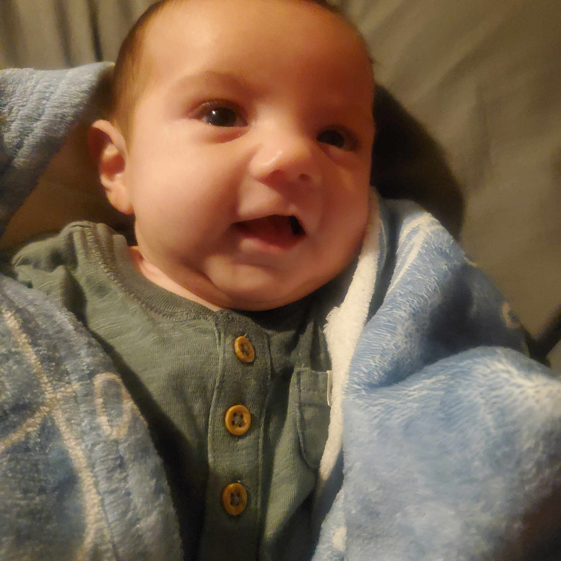 Jack is registered to the contest to win money with this photo: baby, child, face, smile, blanket, clothing, button, green_shirt, blue_blanket, closeup, infant, portrait, cozy, warm, indoors, soft_lighting, cute, young_child, wrapped, happy