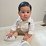 baby, child, toddler, sitting, portrait, indoors, carpet, smiling, serious_expression, slicked_hair, formal_clothing, button_down_shirt, suspenders, beige_pants, white_shoes, sneakers, fashion, floor, wall, home