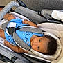 animal_print, baby, blue_onesie, carrying_device, casual, child, curly_hair, fabric, footwear, gray, indoor, infant, looking_up, person, safety_harness, seatbelt, shoe, stroller, texture, white
