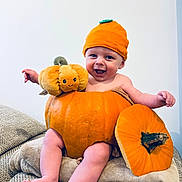 Oscar is registered to the contest to win money with this photo: baby, pumpkin, orange, hat, smile, happy, plush_toy, blanket, cute, infant, child, autumn, seasonal, sitting, cozy, indoor, face, legs, headwear, playful