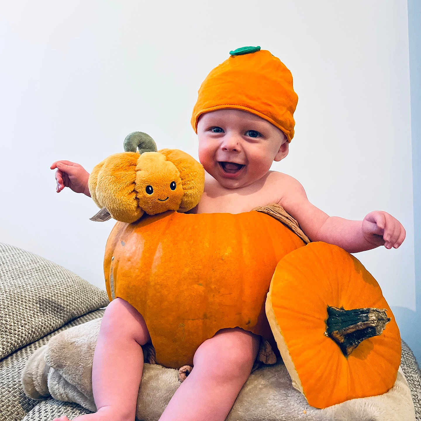 Oscar is registered to the contest to win money with this photo: autumn, baby, blanket, child, cozy, cute, face, happy, hat, headwear, indoor, infant, legs, orange, playful, plush_toy, pumpkin, seasonal, sitting, smile