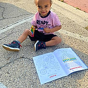 Micah joined the competition — help win amazing prizes! child, toddler, sitting, pavement, coloring_book, toy, striped_shirt, shorts, sneakers, outdoor, sidewalk, sunlight, happy, smiling, playful, person, clothing, casual, young, recreation