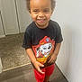 toddler, child, smile, indoor, black_tshirt, red_shorts, curly_hair, carpet, wood_floor, door, wall, sneakers, happy, standing, person, clothing, paw_patrol, marshall, cute, young_child