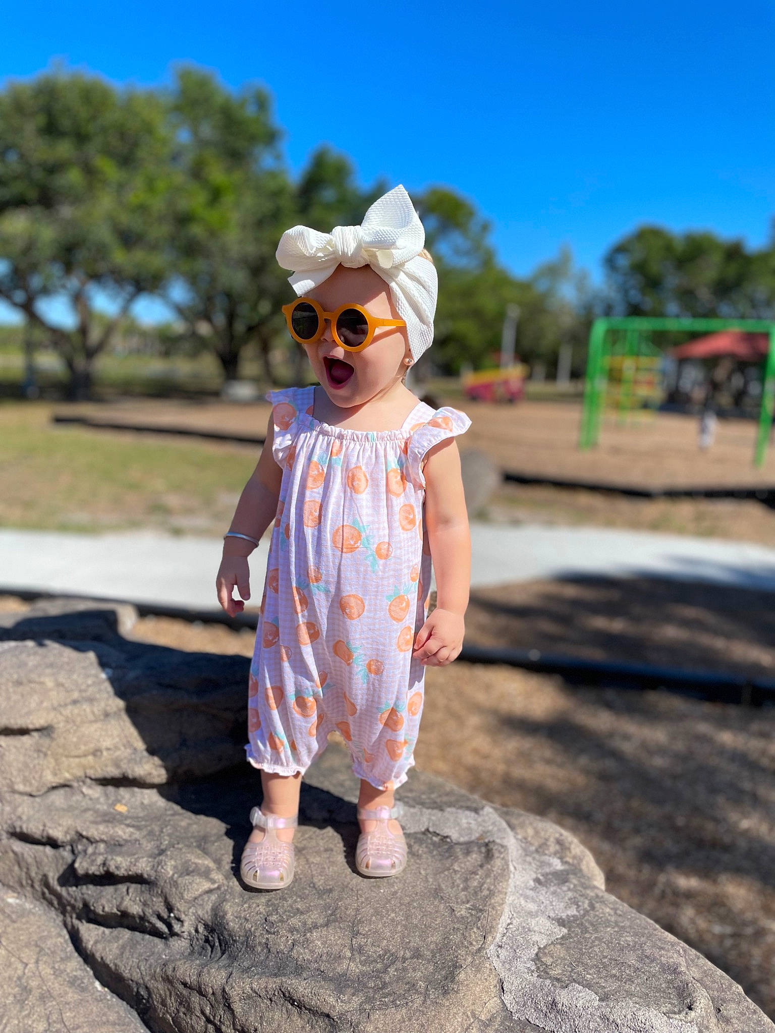 Berklee is registered to the contest to win money with this photo: asphalt, eyewear, glasses, goggles, grass, happy, hat, landscape, leisure, person, plant, recreation, road_surface, sky, summer, sun_hat, sunglasses, toddler, tree, vision_care