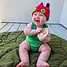 baby, infant, child, smiling, green_outfit, red_hat, plush_blanket, wooden_plaque, sitting, happy, indoors, cute, chubby, feet, hands, face, blue_eyes, hat, floor, wall