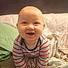 Truen is registered to the contest to win money with this photo: baby, smiling, striped_shirt, bed, blanket, pillow, indoor, child, cute, happy, face, infant, person, soft, cozy, portrait, toddler, clothing, head, warm