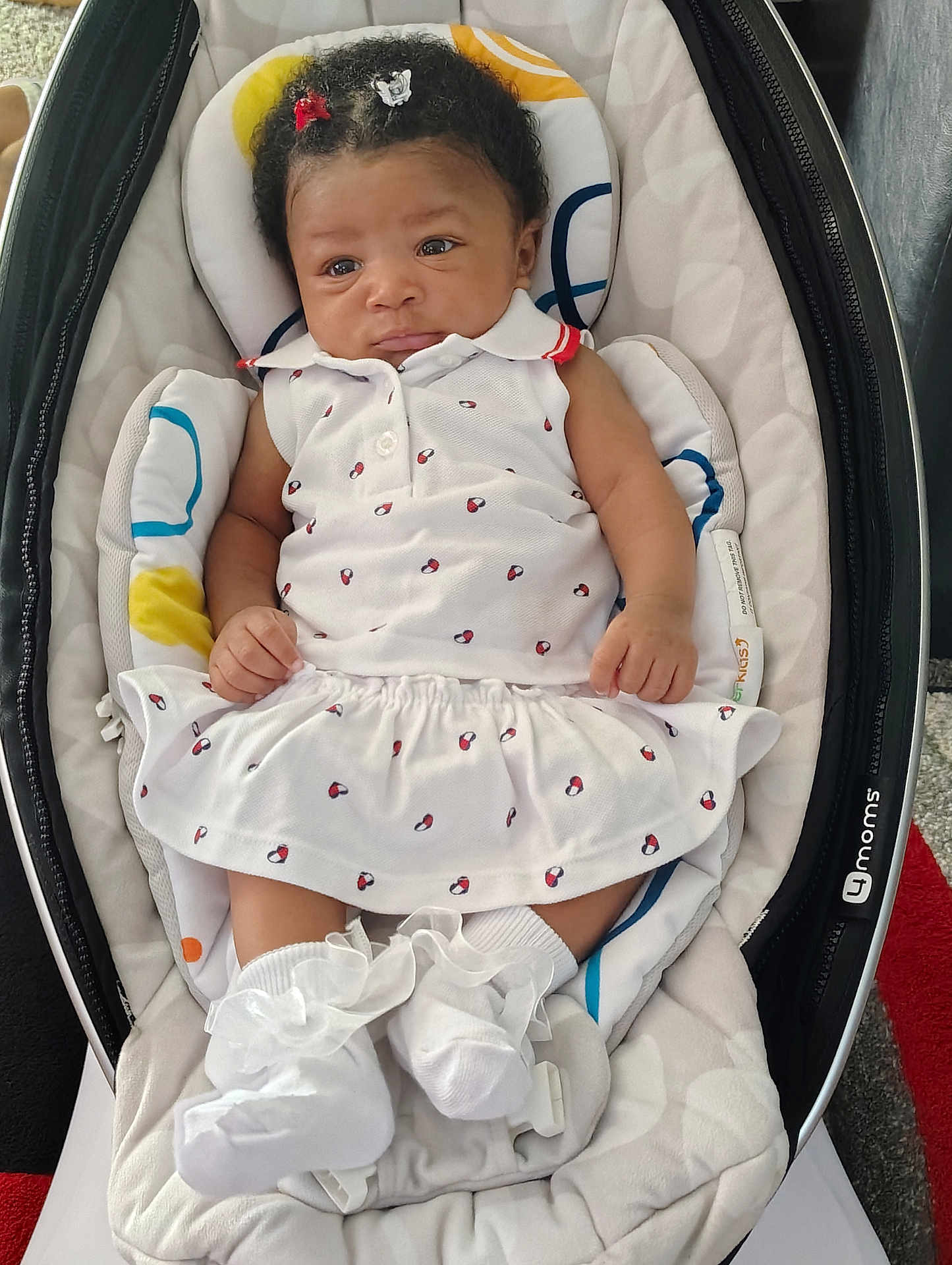 Aiyanna joined the competition — help win amazing prizes! baby, infant, child, white_dress, baby_rocker, cushion, hair_clips, socks, frilly_socks, cute, indoor, carpet, patterned_clothing, infant_fashion, seated, portrait, small_hands, soft_toys, comfortable, resting
