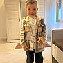 child, boy, indoor, plaid_jacket, pants, smile, standing, wardrobe, window, rug, floor, door, light, clothing, person, portrait, home, young, casual, cozy