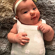 Arden is registered to the contest to win money with this photo: baby, infant, headband, bow, blanket, knitted_dress, flower_pattern, skin, hand, face, cheeks, lying_down, soft_texture, cute, portrait, young_child, indoors, cozy, relaxed, person
