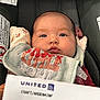 baby, infant, car_seat, bib, clothing, face, eyes, seatbelt, travel_ticket, airline_ticket, hand, text, fabric, seat, transportation, portrait, close_up, indoor, cute, child