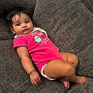 Deanna is registered to the contest to win money with this photo: baby, child, couch, onesie, bracelet, pink_clothing, cupcake_design, curly_hair, indoors, comfortable, cute, portrait, skin, infant, relaxed, furniture, happy, sitting, expression, young