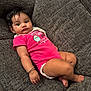 baby, child, couch, onesie, bracelet, pink_clothing, cupcake_design, curly_hair, indoors, comfortable, cute, portrait, skin, infant, relaxed, furniture, happy, sitting, expression, young