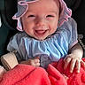 baby, infant, smile, happy, clothing, bonnet, dress, blanket, hand, face, child, cute, indoors, portrait, person, babywear, seat, human, joy, soft
