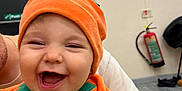 Theo is registered to the contest to win money with this photo: baby, child, costume, orange, pumpkin, smiling, happy, indoor, person, face, headwear, clothing, hand, adult, joy, cute, holding, apparel, infant, portrait