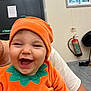 baby, child, costume, orange, pumpkin, smiling, happy, indoor, person, face, headwear, clothing, hand, adult, joy, cute, holding, apparel, infant, portrait
