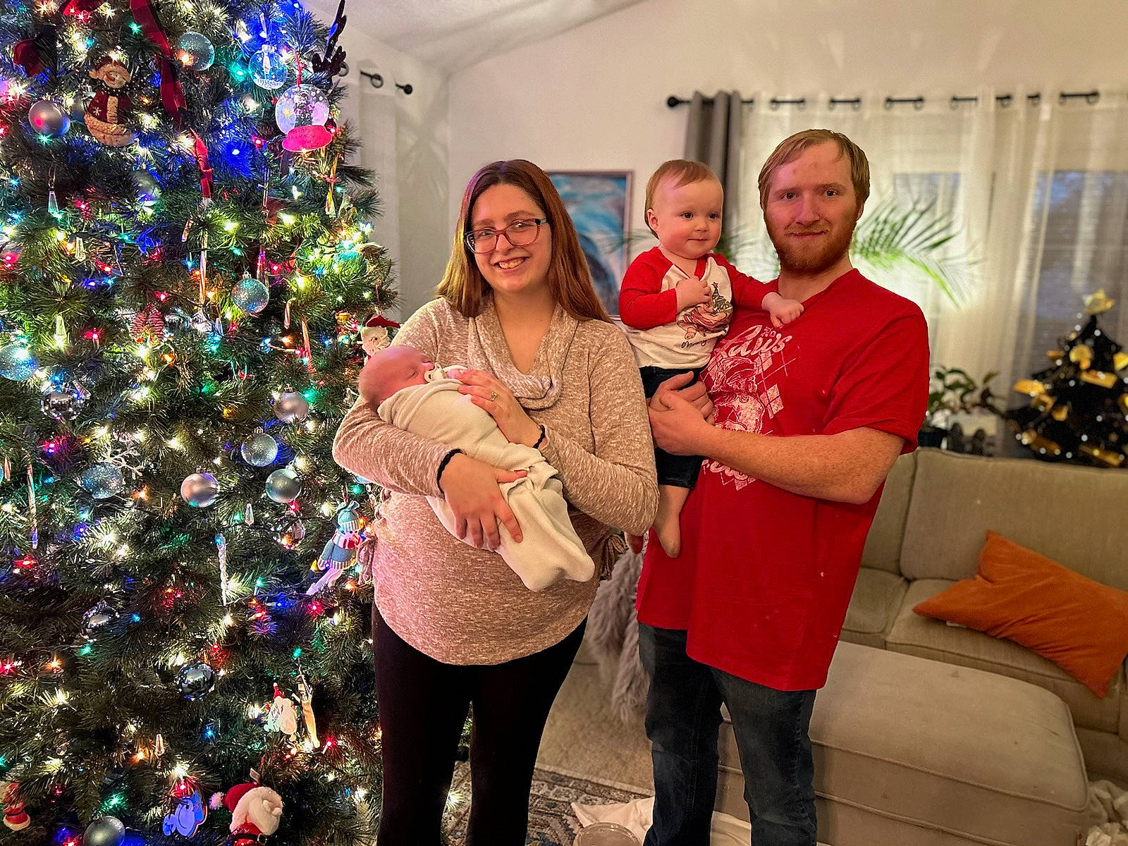 Luella is registered to the contest to win money with this photo: christmas, christmas_decoration, christmas_eve, christmas_ornament, christmas_tree, couch, event, facial_expression, fun, green, happy, holiday, holiday_ornament, joy, lap, ornament, person, plant, room, smile