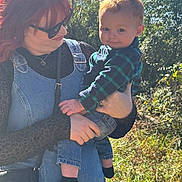 Howard is registered to the contest to win money with this photo: child, toddler, adult, woman, outdoor, forest, trees, sunlight, portrait, family, being_held, smiling, red_hair, sunglasses, overalls, plaid_shirt, denim, boots, nature, daylight
