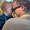 Howard is registered to the contest to win money with this photo: baby, infant, adult, parent, child, face, portrait, outdoor, sunlight, smiling, cuddle, family, bonding, eyeglasses, glasses, beard, plaid_shirt, jacket, close_up, trees