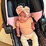 baby, infant, car_seat, headband, bow, smile, clothing, pink, peach, black, seatbelt, infant_wear, footwear, cute, child, indoors, car_seat_cover, person, sitting, adorable