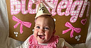 Blakleigh is registered to the contest to win money with this photo: baby, smiling, birthday, party_hat, pink_clothing, 6_months, celebration, happy, infant, child, cute, sitting, indoors, decorations, sign, blanket, face, headwear, festive, joyful